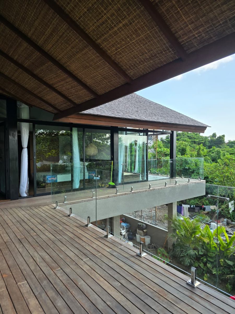 Villa Bali — railing kaca frameless balkon dengan wooden deck dan view hijau